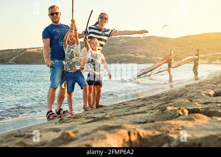 Touristische Familie auf Prasonisi Strand durch blaues plätscherndes Meer und Kitesurfer bei Sonnenuntergang am Horizont am späten Sommertag Griechenland Stockfoto