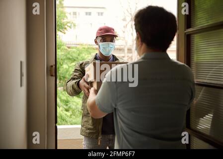 Afrikanischer Kurier in einer Maske, der Pakete an einen Kunden liefert Stockfoto
