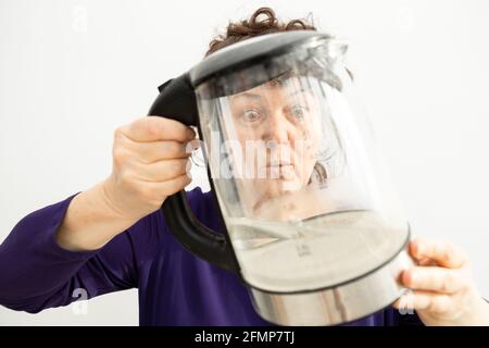 Frau schaut durch einen transparenten Wasserkocher mit Kalk. Kalkablagerungen von Calciumcarbonat. Konzept der Reparatur von Haushaltsgeräten durch Stockfoto