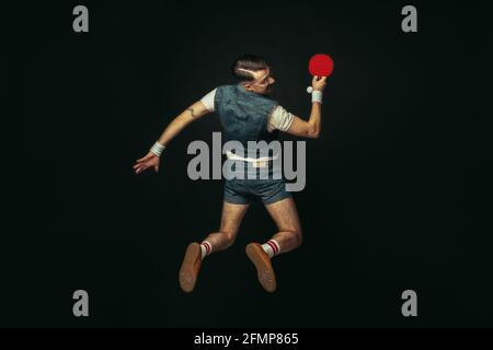 Junger kaukasischer Mann spielt Tennis isoliert auf schwarzem Studiohintergrund im Retro-Stil, Action und Motion-Konzept Stockfoto