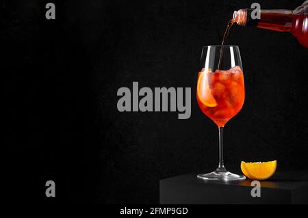 Gießt Aperol Spritz Cocktail in Weinglas mit Eis und Orangenscheibe auf dunklem Hintergrund. Langes kohlensäurehaltiges Getränk. Speicherplatz Kopieren Stockfoto