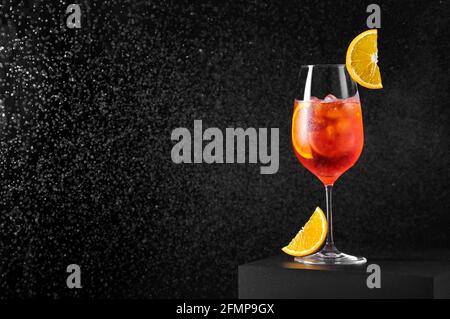 Aperol Spritz Cocktail in Weinglas mit spritzendem Wasser auf dunklem Hintergrund. Langes kohlensäurehaltiges Getränk. Stockfoto