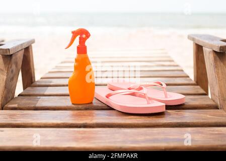 Rosa, lebendige Strandflipflops mit Sonnenschutzcreme, Meereshintergrund. Konzept für einen tropischen Sommerurlaub Stockfoto