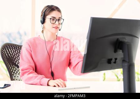 Kundendienstmitarbeiter, die ein Headset trägt, während sie hinter ihrem Computer sitzt und von zu Hause aus arbeitet. Heimbüro. Stockfoto
