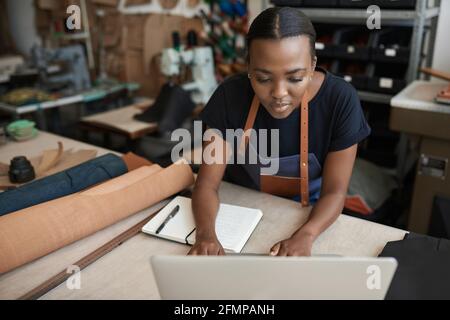 Junge afrikanische Lederarbeiterin mit einem Laptop Stockfoto