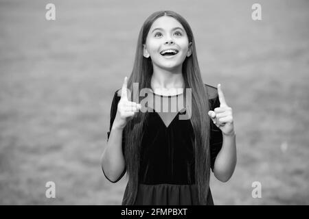Inspiriert glücklich Mädchen mit langen Haaren in Mode Kleid Look up halten indeex Finger angehoben grünen Gras Sommer im Freien, Inspiration Stockfoto