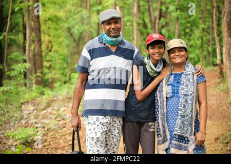 Ein Porträt einer glücklichen 3-köpfigen indischen Familie, die zwischen einem Wald lächelt, nachdem sie eine Wanderung mit Mützen absolviert hat. Stockfoto