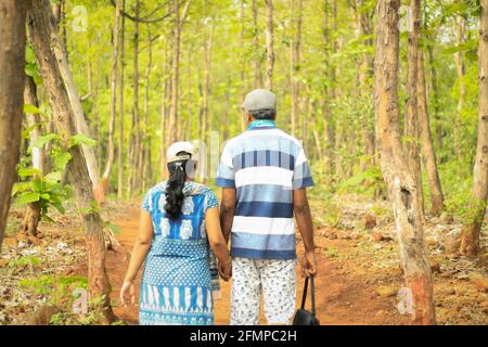 Rückansicht eines Ehepaares mittleren Alters (40-45 Jahre) Gehen Hand in Hand in einem grünen dichten Wald tragen Kappen Stockfoto