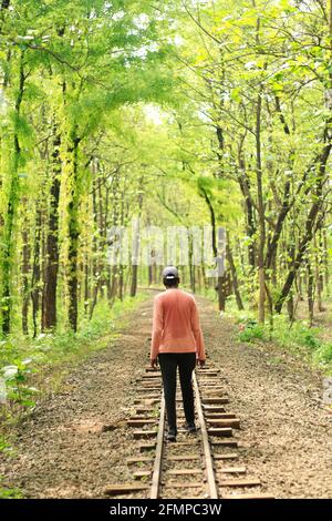 Ein Hinterseitenporträt eines jungen Indianers, der weiter geht Eine Eisenbahnstrecke, die sich in einem dichten grünen Wald befindet Stockfoto