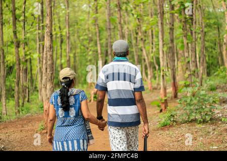 Rückansicht eines Ehepaares mittleren Alters (40-45 Jahre) Gehen Hand in Hand in einem grünen dichten Wald tragen Kappen Stockfoto