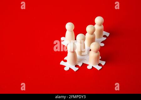 Holzfiguren auf Puzzles auf rotem Hintergrund als Symbol für Teambildung. Organisationsgruppe Mitarbeiter im Geschäft. Zusammenarbeit und Partnerschaft. Stockfoto