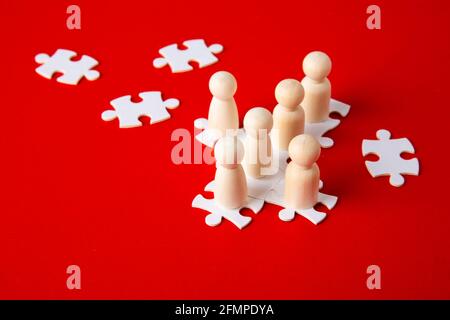 Holzfiguren auf Puzzles auf rotem Hintergrund als Symbol für Teambildung. Organisationsgruppe Mitarbeiter im Geschäft. Zusammenarbeit und Partnerschaft. Stockfoto