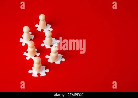 Holzfiguren auf Puzzles auf rotem Hintergrund als Symbol für Teambildung. Organisationsgruppe Mitarbeiter im Geschäft. Zusammenarbeit und Partnerschaft. Stockfoto