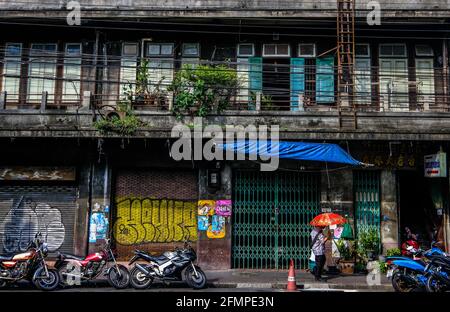 Ein Mann mit einem roten Regenschirm geht an einem alten, mit Graffiti verkleideten Gebäude in der Chinatown-Gegend von Bangkok, Thailand, vorbei Stockfoto