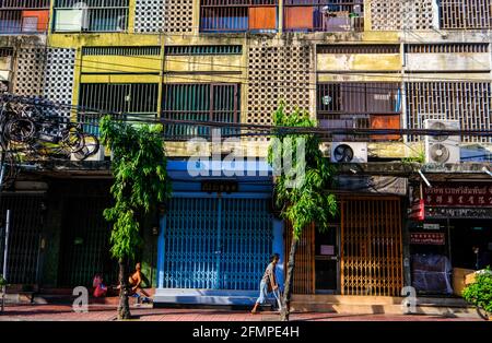 Ein Mann auf Krücken geht an einem bunten Wohnblock in der Chinatown-Gegend von Bangkok, Thailand, vorbei. Stockfoto