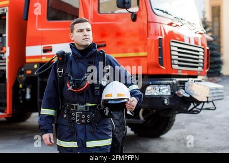 Porträt des kaukasischen Feuerwehrmann in Uniform und Helm in der Nähe des Feuers Motor Stockfoto