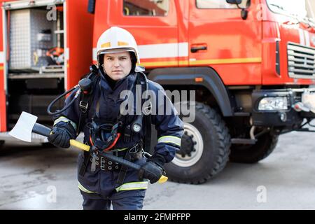 Porträt eines ernsthaften und selbstbewussten kaukasischen Feuerwehrmundes, der im Hintergrund des Staplers eine spezielle Schutzuniform trägt und einen Hammer hält. Stockfoto