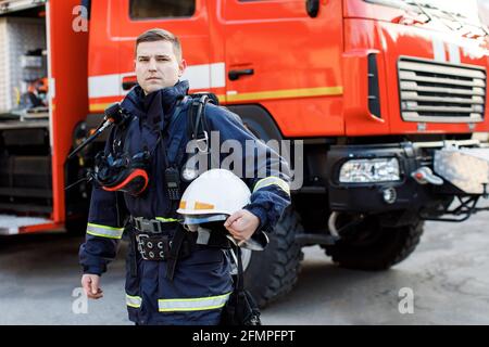 Porträt des kaukasischen Feuerwehrmann in Uniform und Helm in der Nähe des Feuers Motor Stockfoto