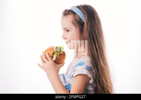 Kleines Mädchen, das großen Burger isst. Kind schaut auf gesunde große Sandwich, Studio isoliert auf weißem Hintergrund. Stockfoto