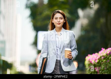 Erfolgreiche junge asiatische weibliche Führungskraft, die auf der Straße hält Eine Tasse Kaffee beim Betrachen der Kamera Stockfoto