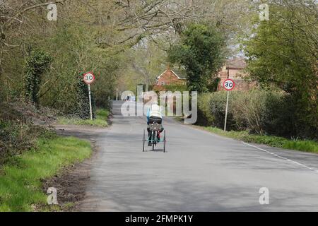 Ein älterer Mann, der ein Dreirad entlang einer Landstraße fährt In Großbritannien Stockfoto