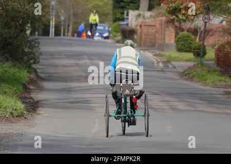 Ein älterer Mann, der ein Dreirad entlang einer Landstraße fährt In Großbritannien Stockfoto