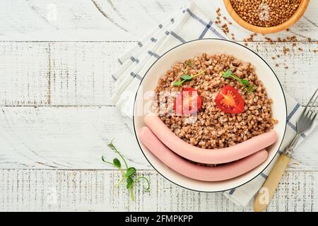 Gekochter Buchweizenbrei, Fleischwürste, Tomate und Mikrogemüse von Erbsen auf einem weißen Teller für das Frühstück oder Mittagessen der Kinder auf steingrauem Hintergrund. Spaß fo Stockfoto