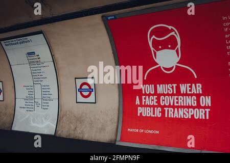 London, Großbritannien - 09. Mai 2021: Schild mit der Abdeckungsanforderung auf dem Bahnsteig der Londoner U-Bahn-Station Kennington. Die Anforderungen wurden eingeführt d Stockfoto