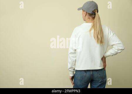Junge Frau in Sweatshirt und Mütze auf beigem Hintergrund Stockfoto