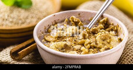 Schüssel Quinoa-Haferbrei, mit Banane, Nüssen und Zimt. Laktosefreies veganes Dessert, süß ohne Milch Stockfoto