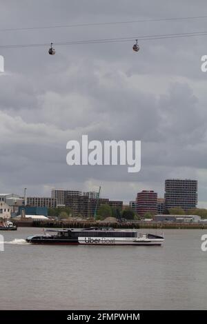 Uber Boat, Thames Clippers, in Greenwich mit der Seilbahn der Emirates Air Line über die Themse in London Stockfoto