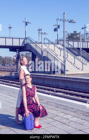 Zwei schöne Frauen im Stil der 1950er Jahre am Bahnhof warten Und die Sonne genießen Stockfoto