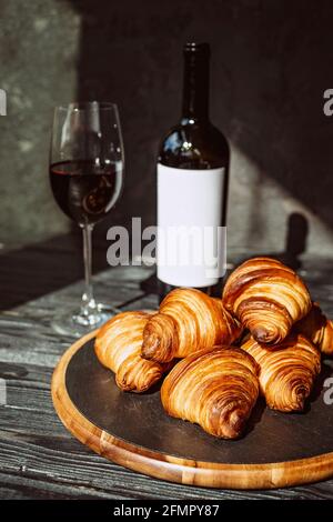 Frisch gebackene duftende Croissants auf einem schwarzen Steinbrett, ein Glas Rotwein und eine Flasche. Romantisches Abendessen. Stockfoto