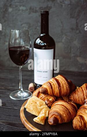 Frisch gebackene, duftende Croissants mit Hartkäse auf einem schwarzen Steinbrett, einem Glas Rotwein und einer Flasche. Romantisches Abendessen. Stockfoto