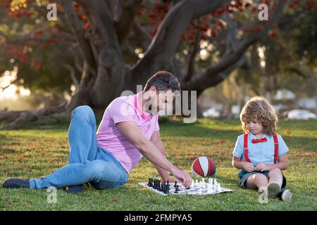 Sohn liegt auf Gras und spielt Schach mit Vater. Schachschule für Kinder. Stockfoto