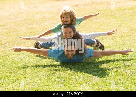 Familie liegt auf Gras im Park. Fly-Konzept, kleiner Junge sitzt Pickaback, während der Flug imitiert. Stockfoto