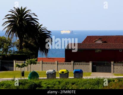 Eine Reihe von Mülltonnen für allgemeine Glasabfälle aus Kunststoff und papr mit Blick auf das Meer und ein Schiff, das den Hafen von Santander Cantabria Spanien verlässt Stockfoto