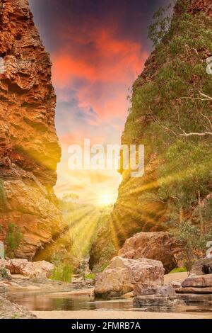 Sonnenaufgang in der Simpsons Gap Gorge in den West MacDonnell Ranges Im Northern Territory von Australien mit roten steilen Felsen und Sonne mit hellen Sonnenstrahlen Stockfoto
