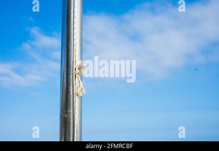 Seilknoten auf silbernem Pol mit blauem Himmel auf dem Strand Stockfoto