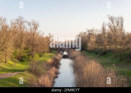 Landschaft des Flusskanals der Stadt, im Hintergrund die Brücke. Frühlingslandschaft. Klimawandel in der Ukraine. Stockfoto