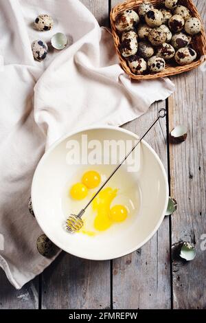 Zerbrochene Wachteleier in einer Schüssel auf einem hölzernen Hintergrund. Stockfoto