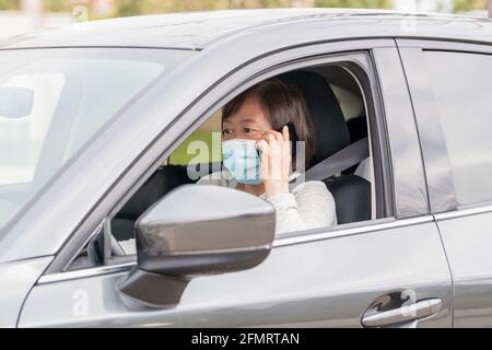 Reife asiatische Frau in einem Auto, die am Telefon spricht: Selektiver Fokus. Stockfoto