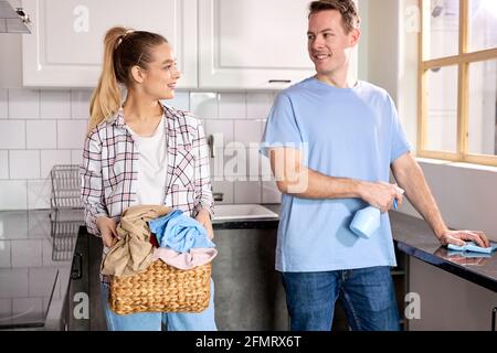 Hausarbeit, junges Ehepaar zu Hause, Reinigung der Küche mit Reinigungsmitteln, gehen, um Dinge zu waschen. Kaukasischer Mann und Frau in legerer Kleidung Housekeeping Stockfoto