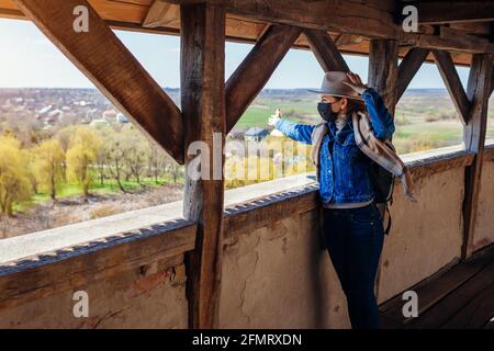 Fröhlicher Tourist, der auf dem Balkon von Schloss Olesko spazieren geht und die Frühlingslandschaft mit Maske während der Coronavirus-Covid-19-Pandemie bewundert. Reisen in der westlichen Ukra Stockfoto