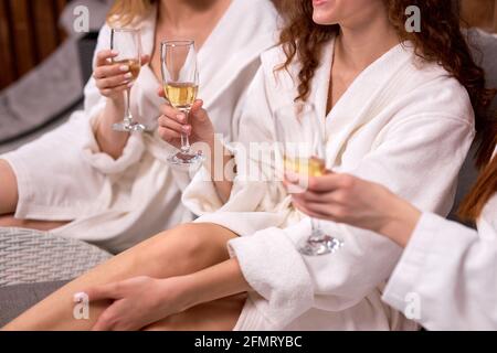 Elegante, charmante Frauen, die ein Glas Champagner in der Hand halten, genießen eine tolle Zeit im Spa Resort Hotel, ein Nahaufnahme-Foto der Hände, kurzgeschnittene Damen im Bademantel Stockfoto