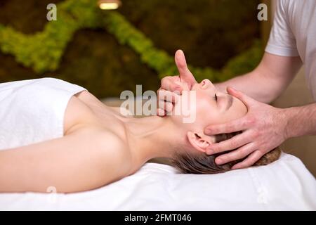 Seitenansicht einer entspannten Frau, die Gesichtsmassage genießt. Männlicher Therapeut, der Kopf- und Nackenmassage für weibliche Klientin macht. Professionelle Masseur.Entspannung, beaut Stockfoto