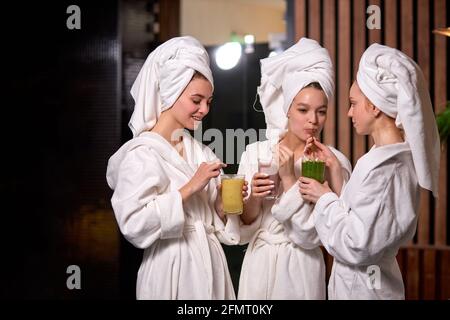Junge Frauen entspannen und trinken saftige Getränke-Smoothies in Roben während des Wellness-Wochenendes im Wellness-Center, nach Spa-Behandlungen reden Stockfoto