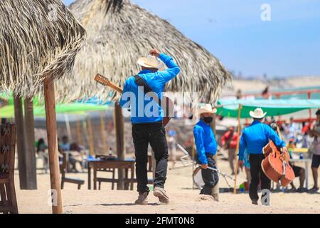 Musiker oder nördliches Popmusik-Ensemble laufen auf dem Sand in einer Palapa-Gegend und legen am Strand oder an der Kino Bay an. Hermosillo, Sonora, Mexiko. Altes Kino. Touristisches Ziel, (Foto von Luis Gutierrez / Norte Photo) Musicos o conjunto de musica popular norteña camina por la Arena en area de palapa y muelle de la playa o Bahía de Kino . Hermosillo, Sonora, Mexiko. Kino viejo. Destino Turistico, (Foto von Luis Gutierrez / Norte Photo) Stockfoto