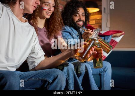 Seitenansicht auf aufgeregte Freunde, die beim Sportspiel-Wettbewerb im Fernsehen Bierflaschen anklirren, die beste amerikanische Mannschaft anfeuern und das Tor antizipieren. Fokus Stockfoto