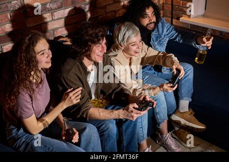 Paare Freunde halten Joystick spielen Videospiel auf der Konsole, um Spaß zu haben, entspannt sitzen. Fröhliche Männer und Frauen in legerer Kleidung verbringen Zeit miteinander Stockfoto
